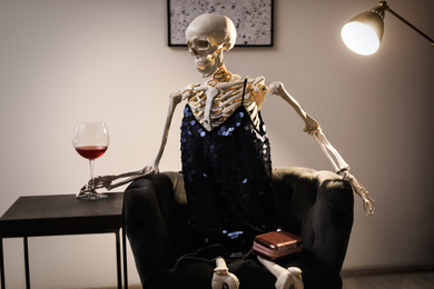 Skeleton in dress with wine sitting at table indoors