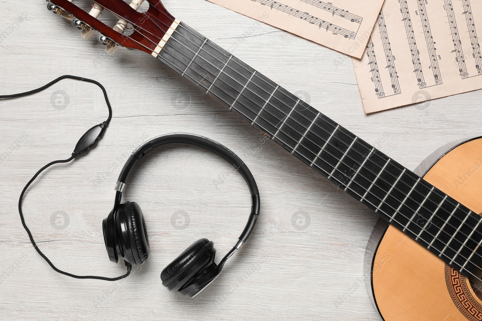 Photo of Composition with guitar and music notations on light wooden table, flat lay