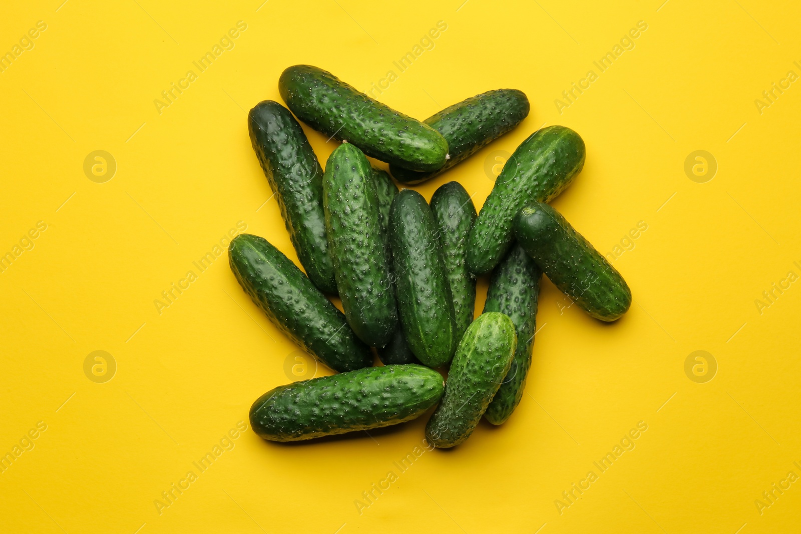 Photo of Heap of fresh ripe cucumbers on yellow background, flat lay