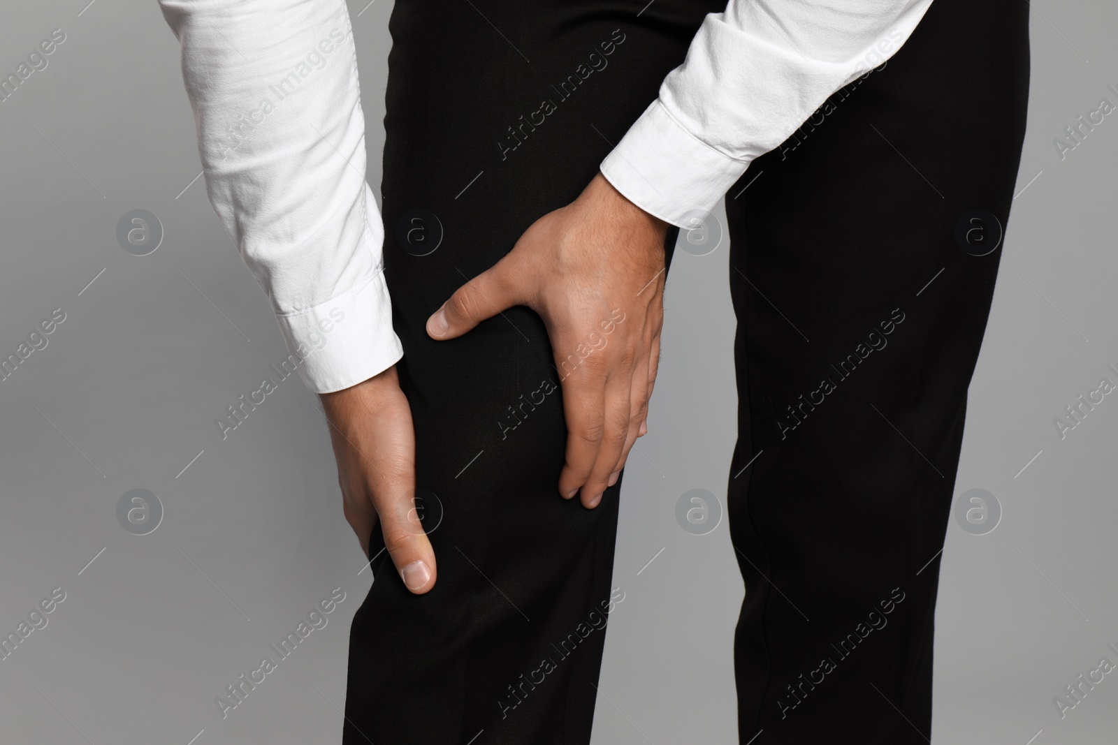 Photo of Businessman suffering from knee pain on light grey background, closeup