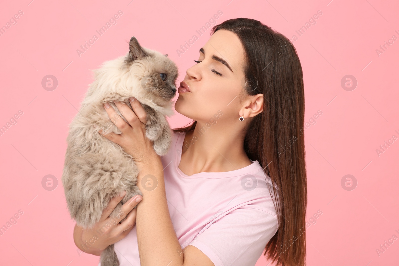 Photo of Woman kissing her cute cat on pink background