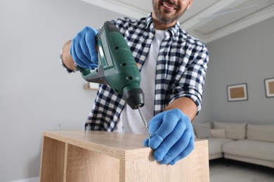 Photo of Man with electric screwdriver assembling furniture at home, selective focus
