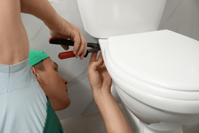 Photo of Professional plumber repairing toilet bowl in bathroom