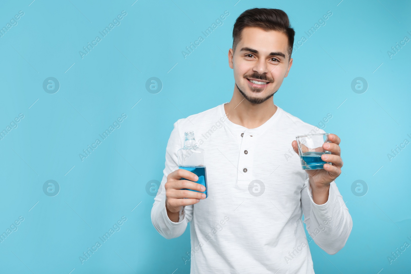 Photo of Young man holding bottle and glass with mouthwash on color background, space for text. Teeth and oral care