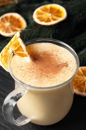 Photo of Glass cup of delicious eggnog with dried orange slice and cinnamon on gray table, closeup