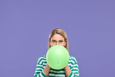 Woman blowing up balloon on violet background