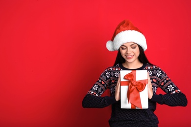 Young beautiful woman in Santa hat with gift box on color background. Christmas celebration