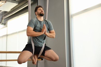 Photo of Young man meditating in fly yoga hammock indoors