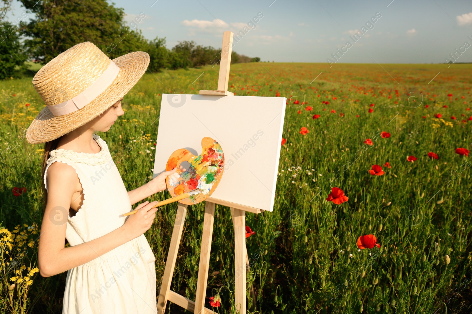 Photo of Little girl painting on easel in beautiful poppy field