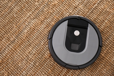 Photo of Modern robotic vacuum cleaner on brown rug, top view. Space for text