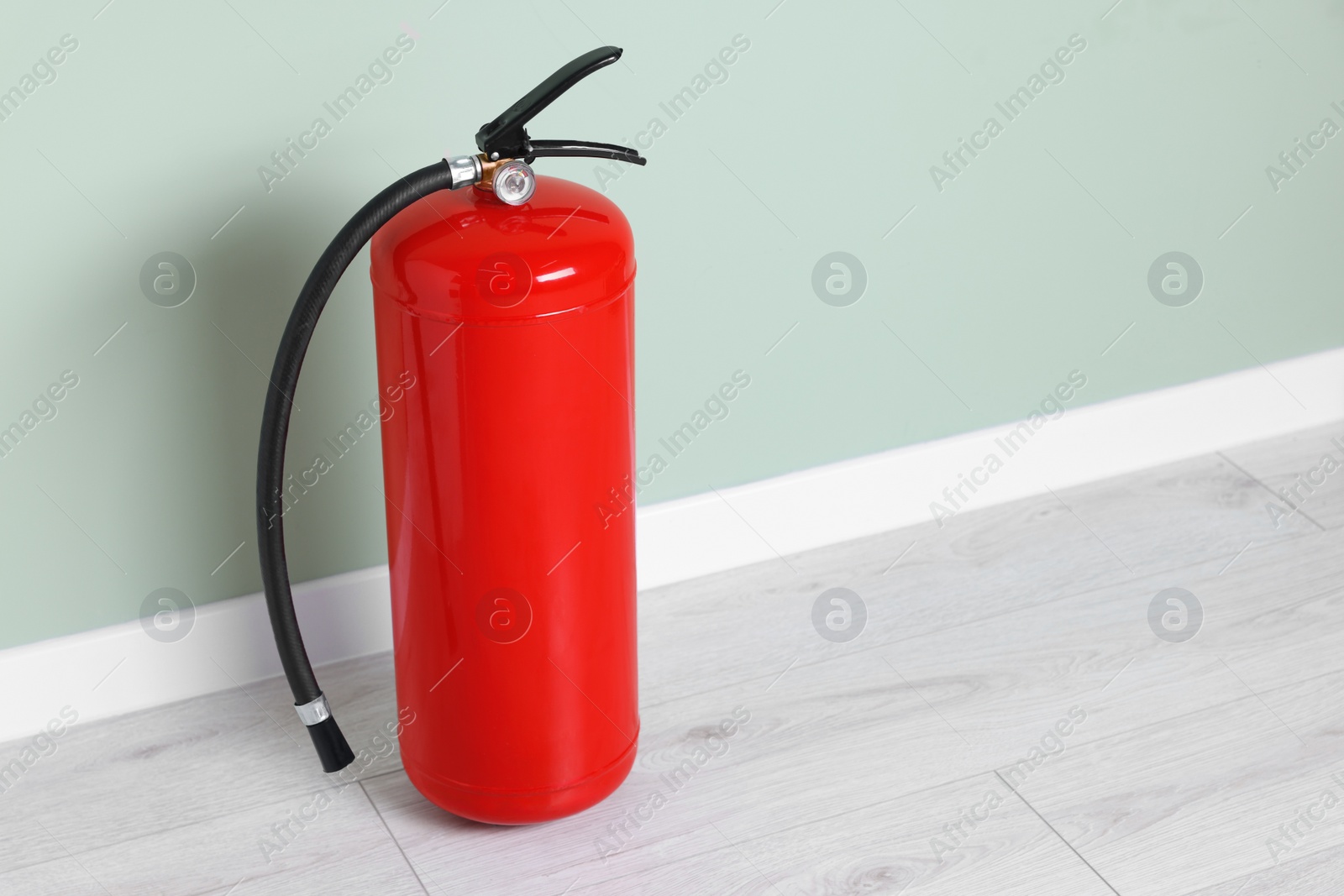 Photo of Red fire extinguisher near light green wall. Space for text