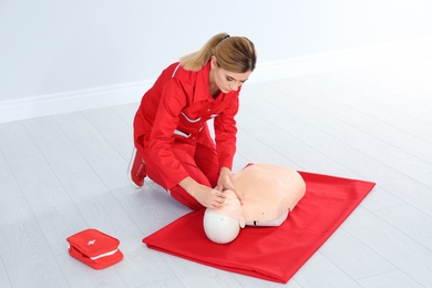 Photo of Woman in uniform practicing first aid on mannequin indoors