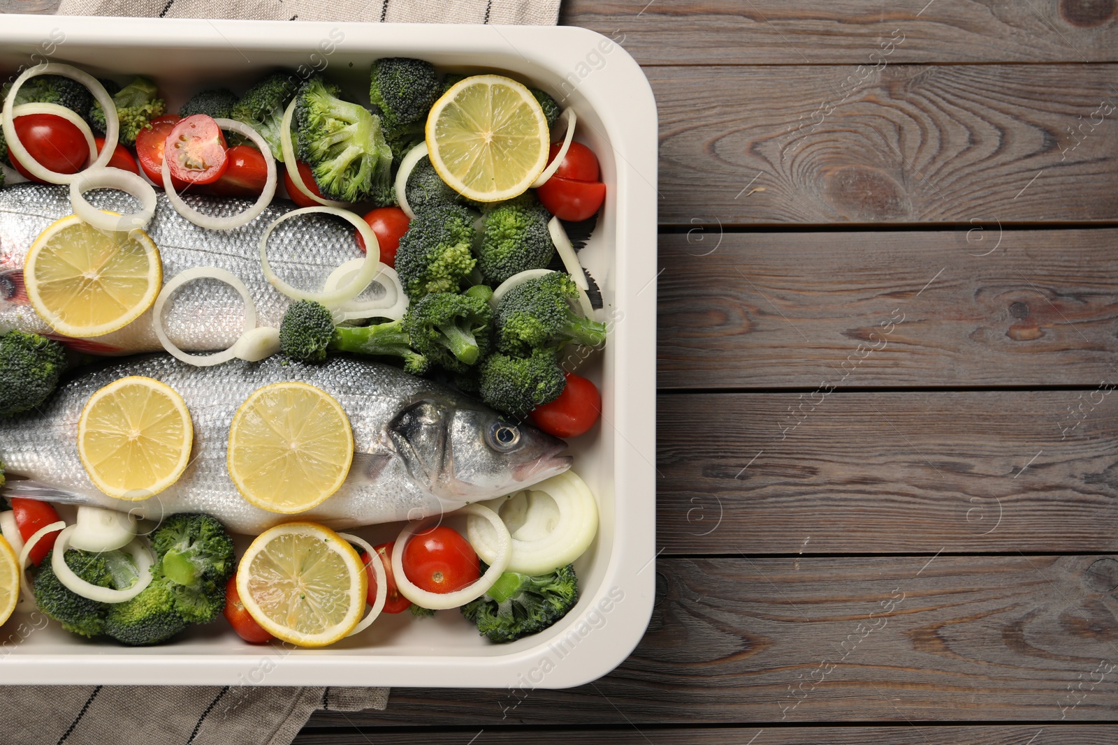 Photo of Raw fish with vegetables and lemon in baking dish on wooden table, top view. Space for text