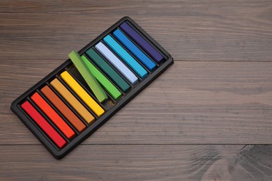 Photo of Colorful pastels in tray on wooden table, space for text. Drawing materials