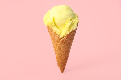 Photo of Delicious yellow ice cream in waffle cone on pink background