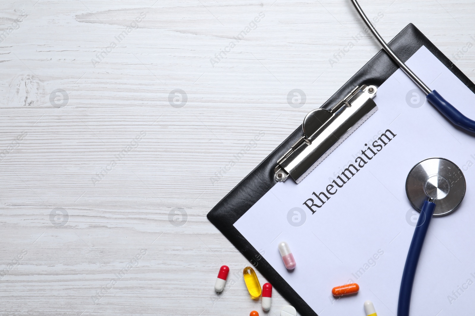 Photo of Clipboard with word Rheumatism, stethoscope and pills on white wooden table, flat lay. Space for text