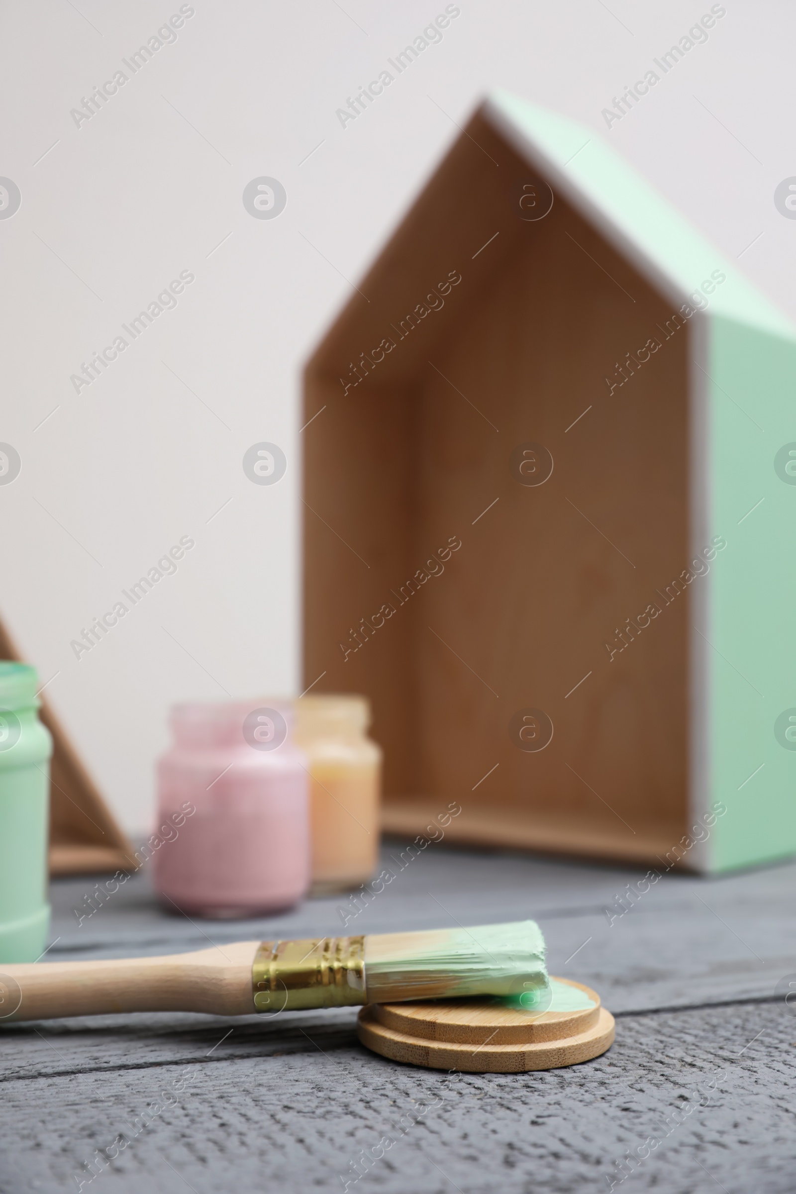 Photo of Brush with paint and model of house on grey wooden table