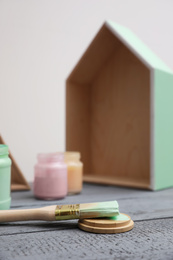 Photo of Brush with paint and model of house on grey wooden table