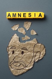 Photo of Yellow cubes with word Amnesia and human head with brain pieces made of crumbled paper on grey background, flat lay