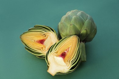 Photo of Cut and whole fresh raw artichokes on green background, closeup