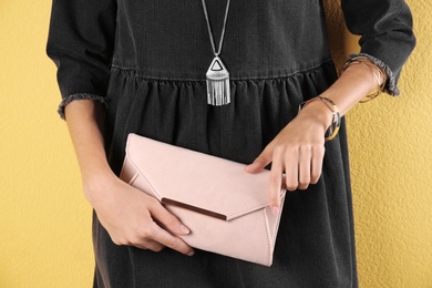 Young woman in stylish outfit with purse on color background, closeup