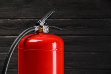 Photo of Fire extinguisher against wooden wall, closeup. Space for text