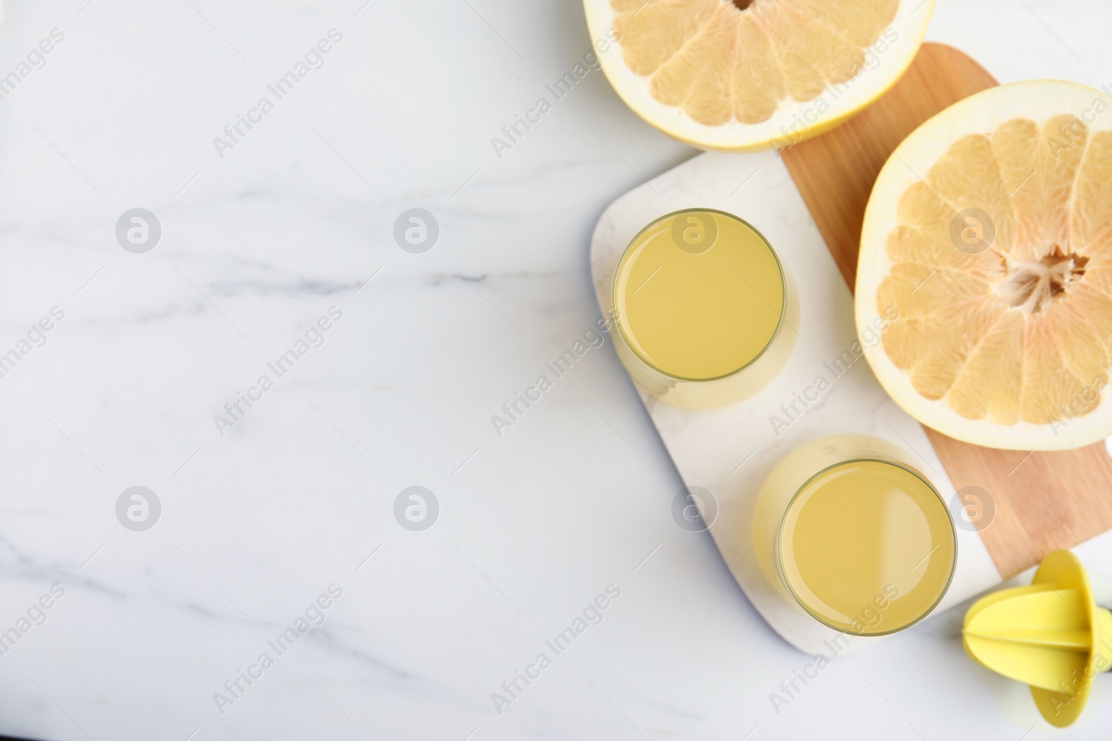 Photo of Glasses of fresh pomelo juice with reamer and fruit on white marble table, flat lay. Space for text