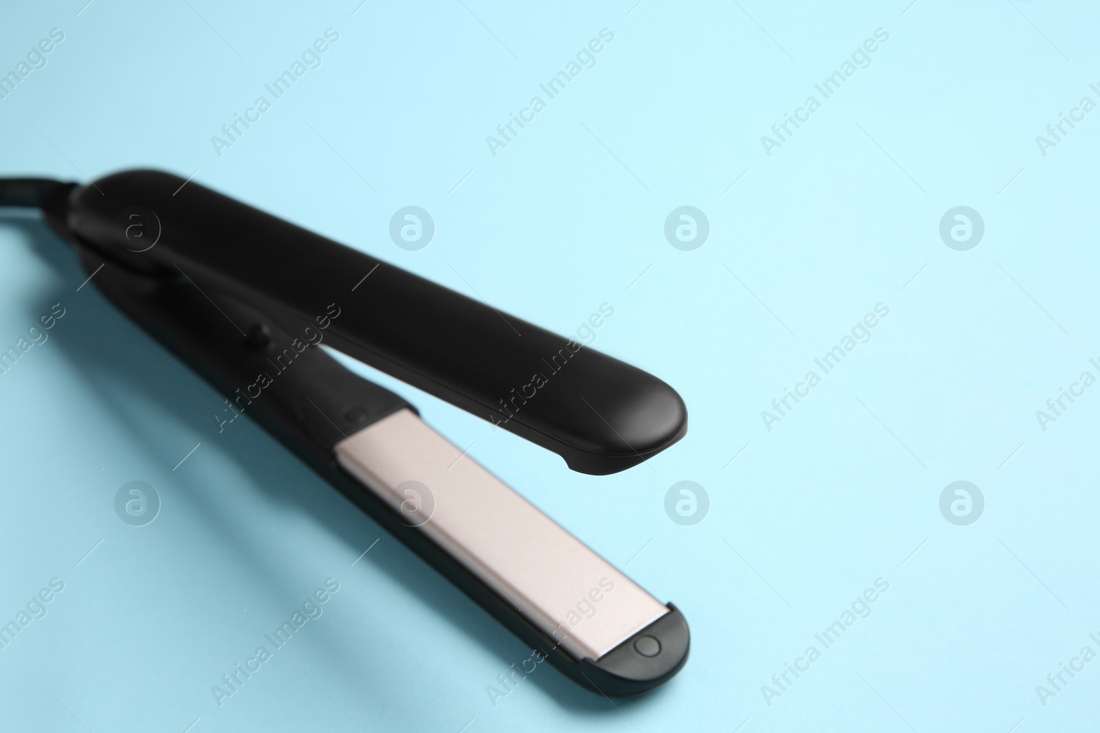 Photo of Modern flat hair iron on light blue background, closeup