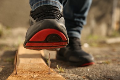 Careless worker stepping on nail in wooden plank outdoors, closeup