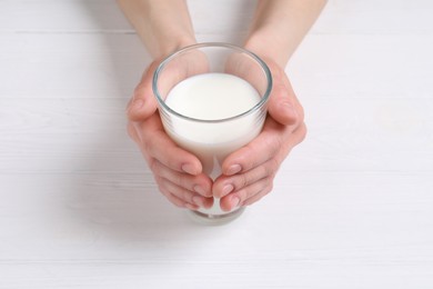 Photo of Woman holding glass of milk at white wooden table, closeup