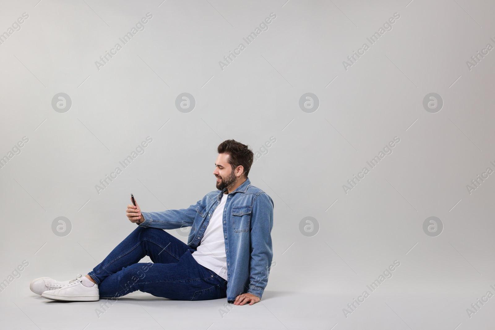 Photo of Handsome young man using smartphone on grey background, space for text