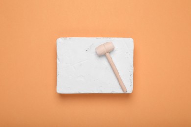 Photo of Educational toy for motor skills development. Excavation kit (plaster and wooden mallet) on orange background, top view