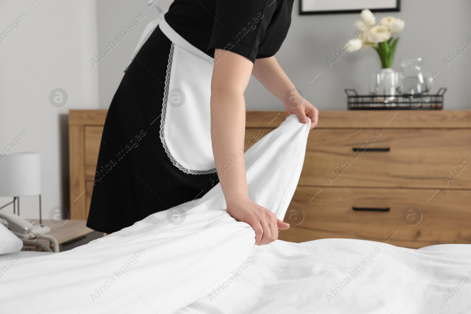 Photo of Chambermaid making bed in hotel room, closeup