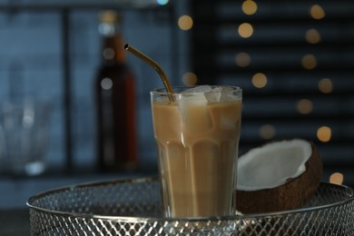 Glass of iced coffee and coconut on metal tray against blurred lights, closeup