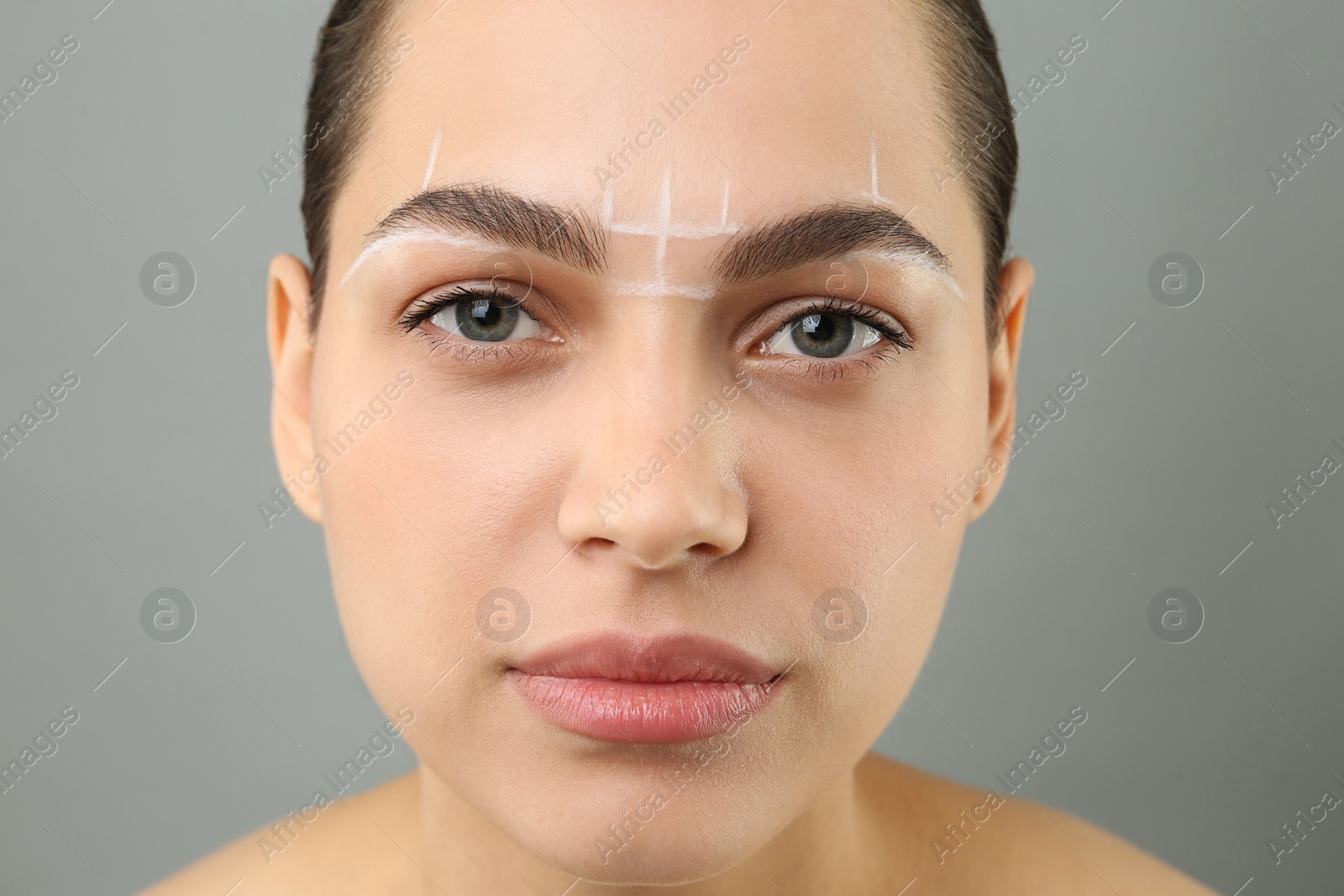 Photo of Eyebrow correction. Young woman with markings on face against grey background