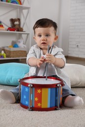 Cute little boy with toy drum and drumsticks at home