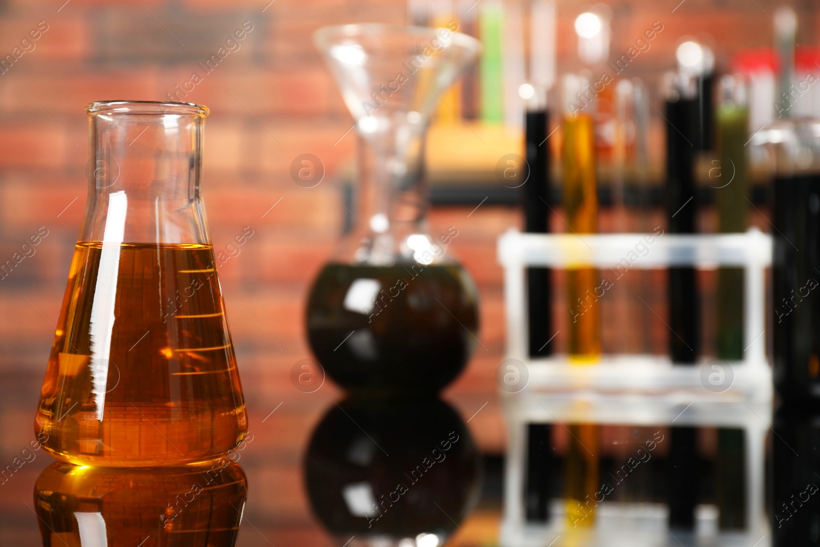 Photo of Laboratory glassware with different types of oil on mirror table indoors, closeup