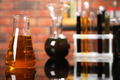 Photo of Laboratory glassware with different types of oil on mirror table indoors, closeup