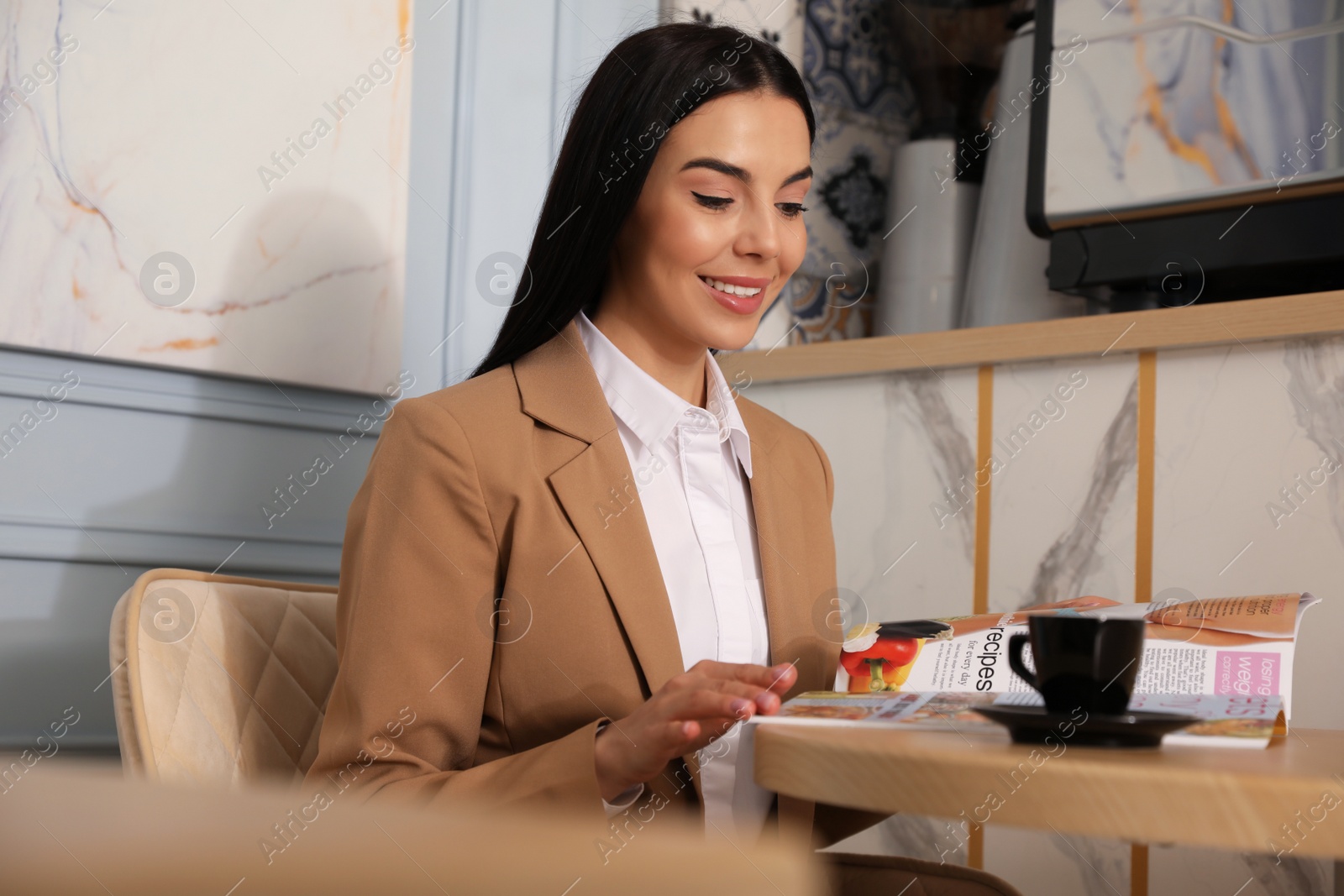 Photo of Woman with cup of coffee reading magazine at cafe in morning