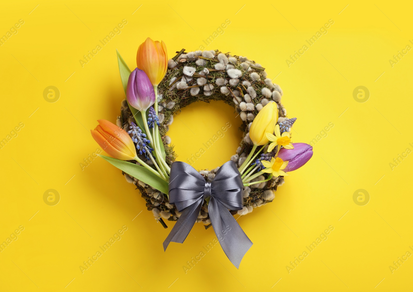 Photo of Willow wreath with different beautiful flowers and grey bow on yellow background, top view