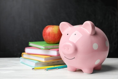 Piggy bank with stack of books and apple on table