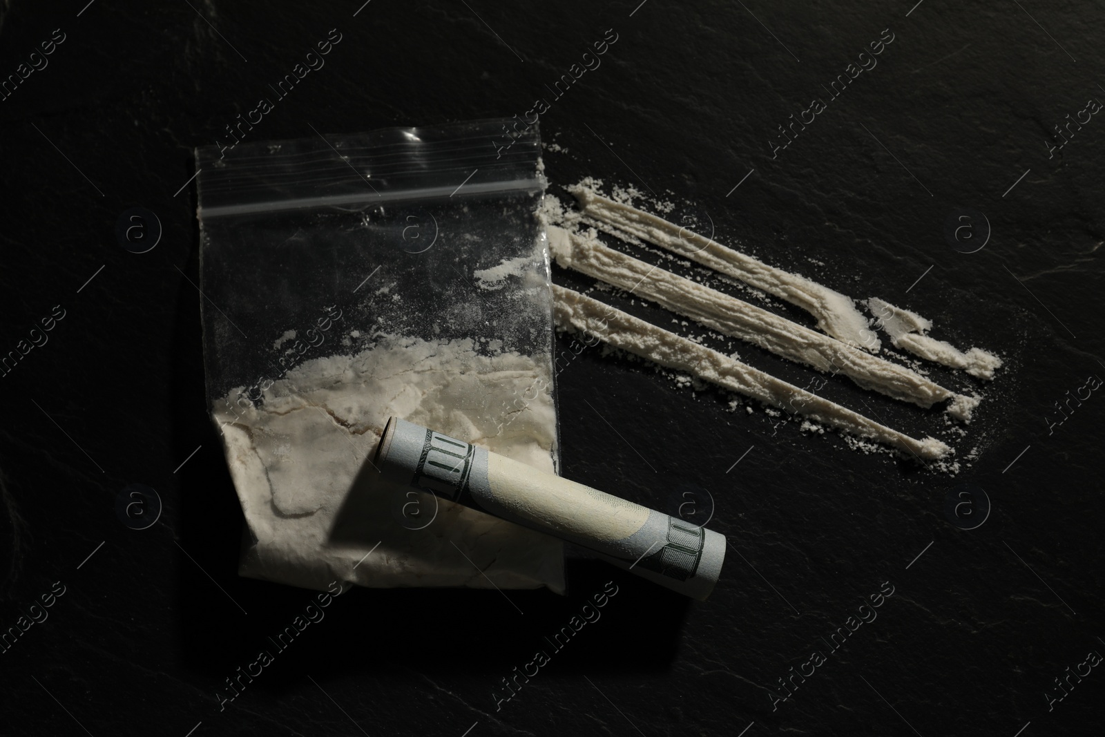 Photo of Drug addiction. Plastic bag with cocaine and rolled dollar banknote on dark textured background, flat lay