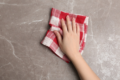 Woman wiping brown marble table with kitchen towel, top view