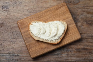 Photo of Slice of bread with tasty cream cheese on wooden table, top view