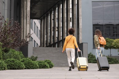 Photo of Being late. Women with suitcases walking towards building outdoors, back view