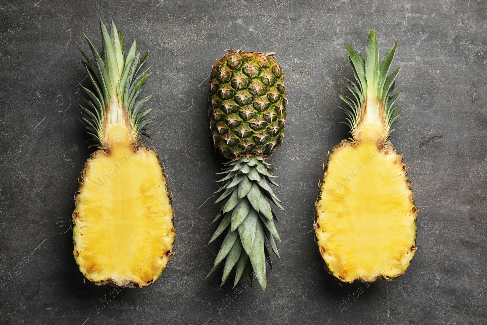 Photo of Fresh whole and cut pineapples on black stone background, top view