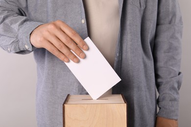 Photo of Man putting his vote into ballot box on light grey background, closeup