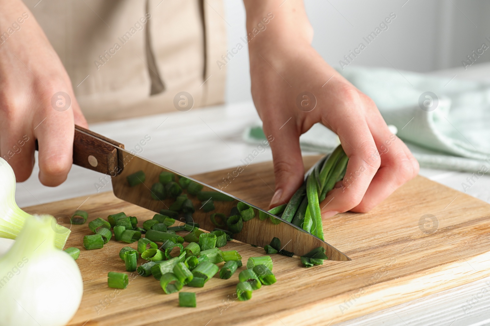 Photo of Woman cutting fresh green onion on wooden board at table, closeup