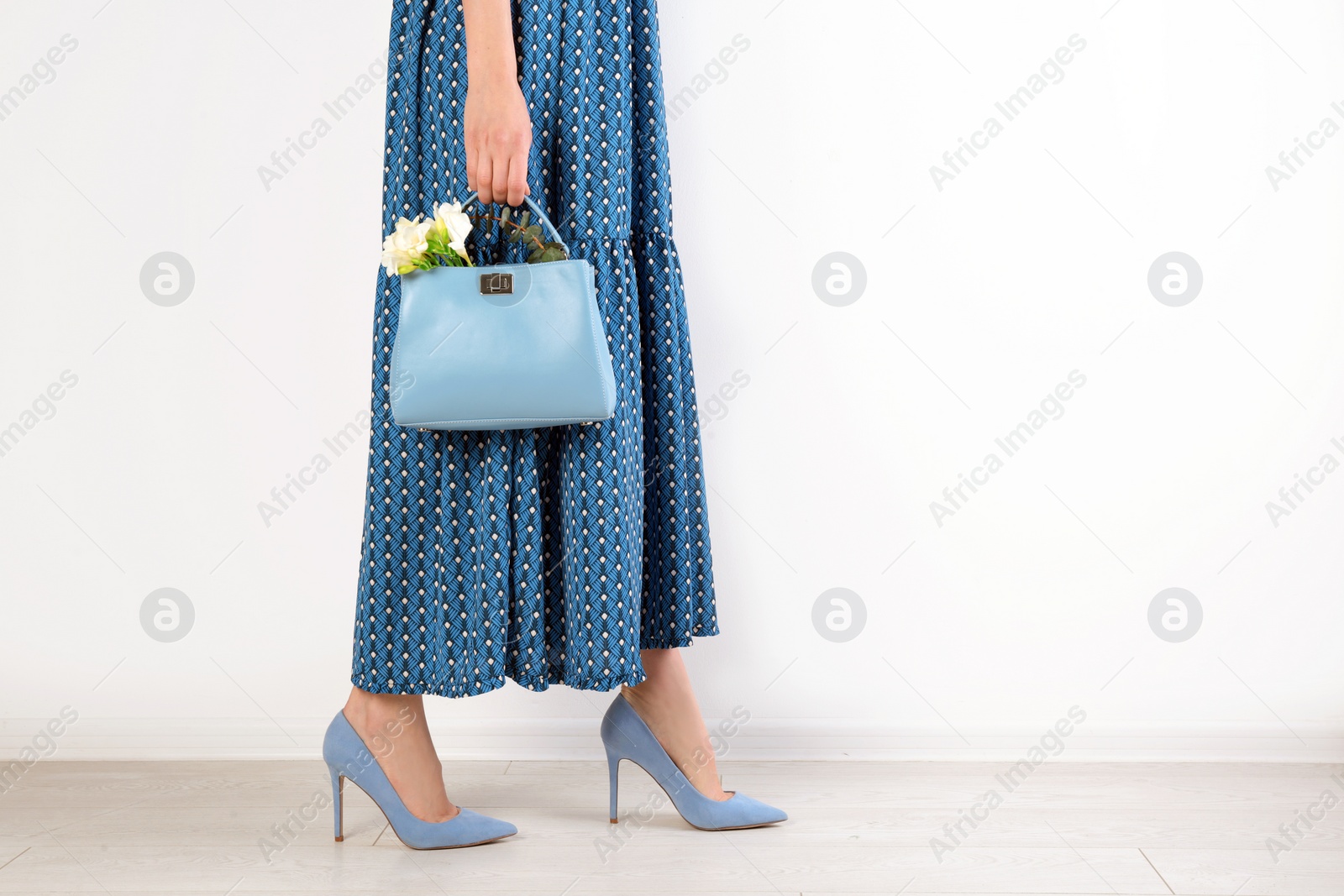 Photo of Stylish woman with handbag and spring flowers near light wall. Space for text
