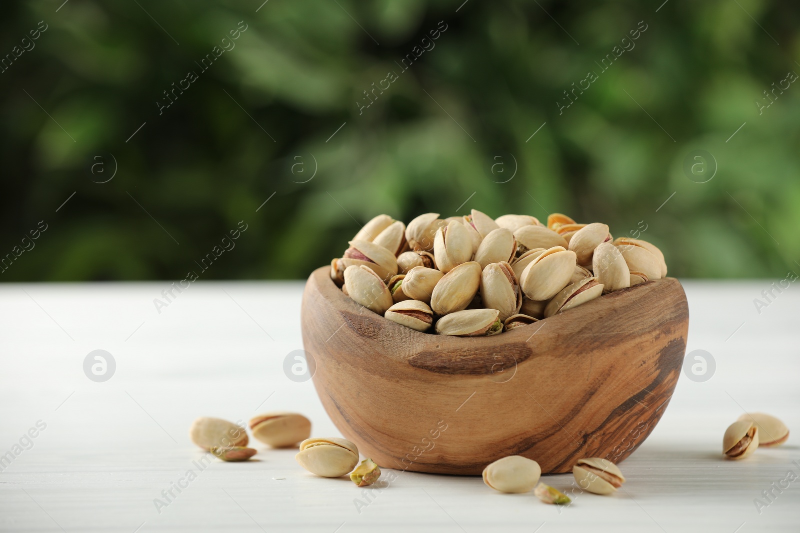 Photo of Tasty pistachios in bowl on white table against blurred background. Space for text